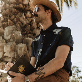 fit model writing in his sketchbook in The Embroidered Short Sleeve Western in Indigo Linen