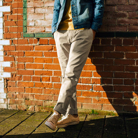 fit model wearing The Democratic Foundation Pant in Organic Stone leaning against a brick wall