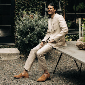 fit model sitting on a wooden table in The Sheffield Trouser in Natural Linen