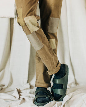 material shot of The Atelier and Repairs Chino in British Khaki, legs crossed on model, Bottoms by Taylor Stitch