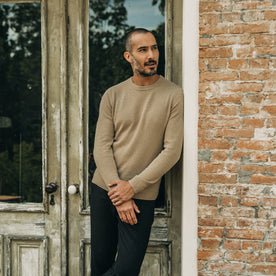 fit model leaning against the wall wearing The Lodge Sweater in Camel