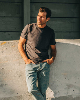 our fit model wearing The Standard Issue Tee in Charcoal Hemp—leaning against wall, Knits by Taylor Stitch