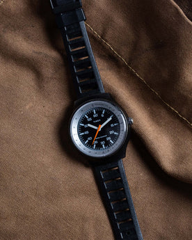 flatlay of the 1977 Timex Black Max on a brown background, Accessories by Taylor Stitch