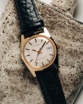 flatlay of the 1978 Timex Gold Marlin on a ceramic background, Accessories by Taylor Stitch