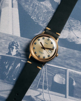 flatlay of the 1975 Timex Viscount against old photographs, Accessories by Taylor Stitch