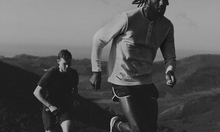 Black and white photo of two guys running, with mountain scenery in the background.