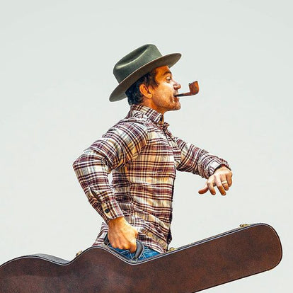 A man walking with a guitar while smoking a pipe