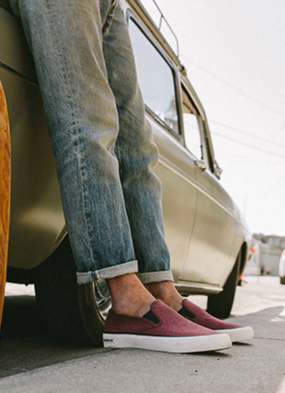 Man in our maroon slip on sneakers leaning against a car