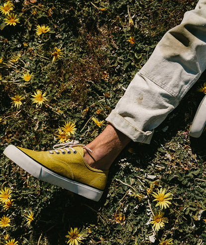 Man in jeans wearing our yellow SeaVeesxTS sneaker in a daisy field