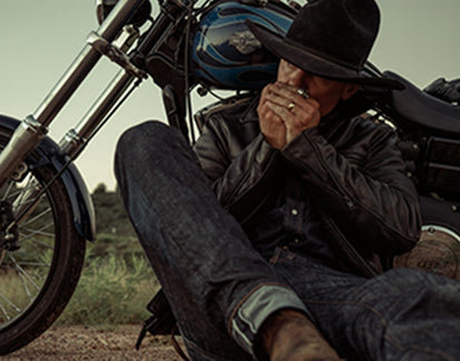 Man whistling with hands while sitting up against his motorcycle