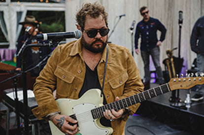 Nate Rateliff playing the guitar on stage in our collaboration piece the Lined Long Haul Jacket in Sand Suede