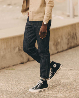 fit model leaning against the wall wearing The Democratic Jean in Rigid Organic Selvedge, Bottoms by Taylor Stitch