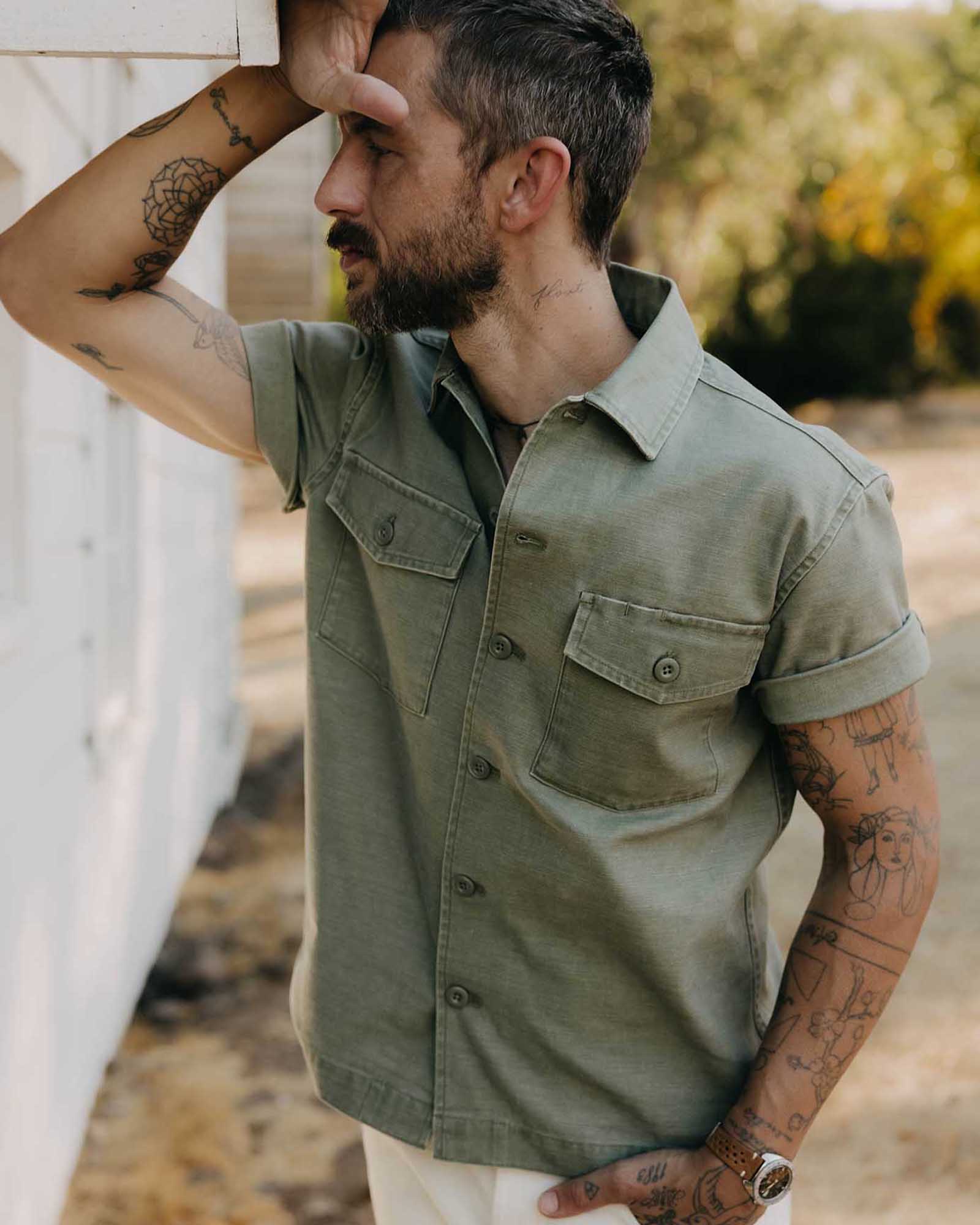 fit model leaning against the wall wearing The Short Sleeve Surplus Shirt in Field Olive Reverse Sateen, Wovens by Taylor Stitch