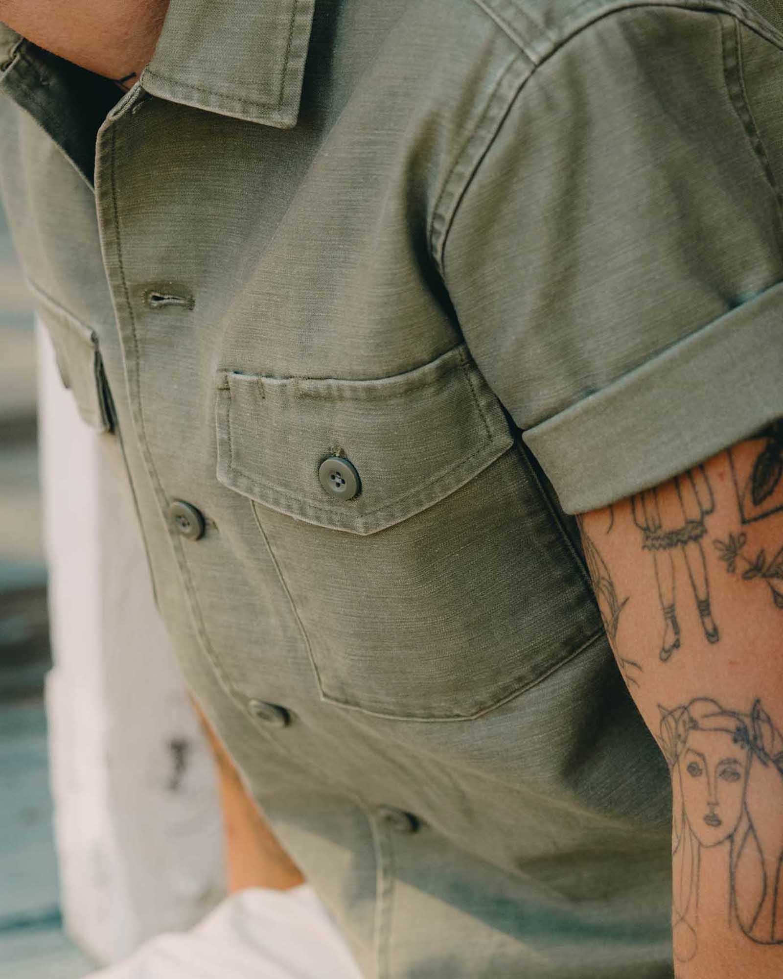 fit model sitting wearing The Short Sleeve Surplus Shirt in Field Olive Reverse Sateen, Wovens by Taylor Stitch