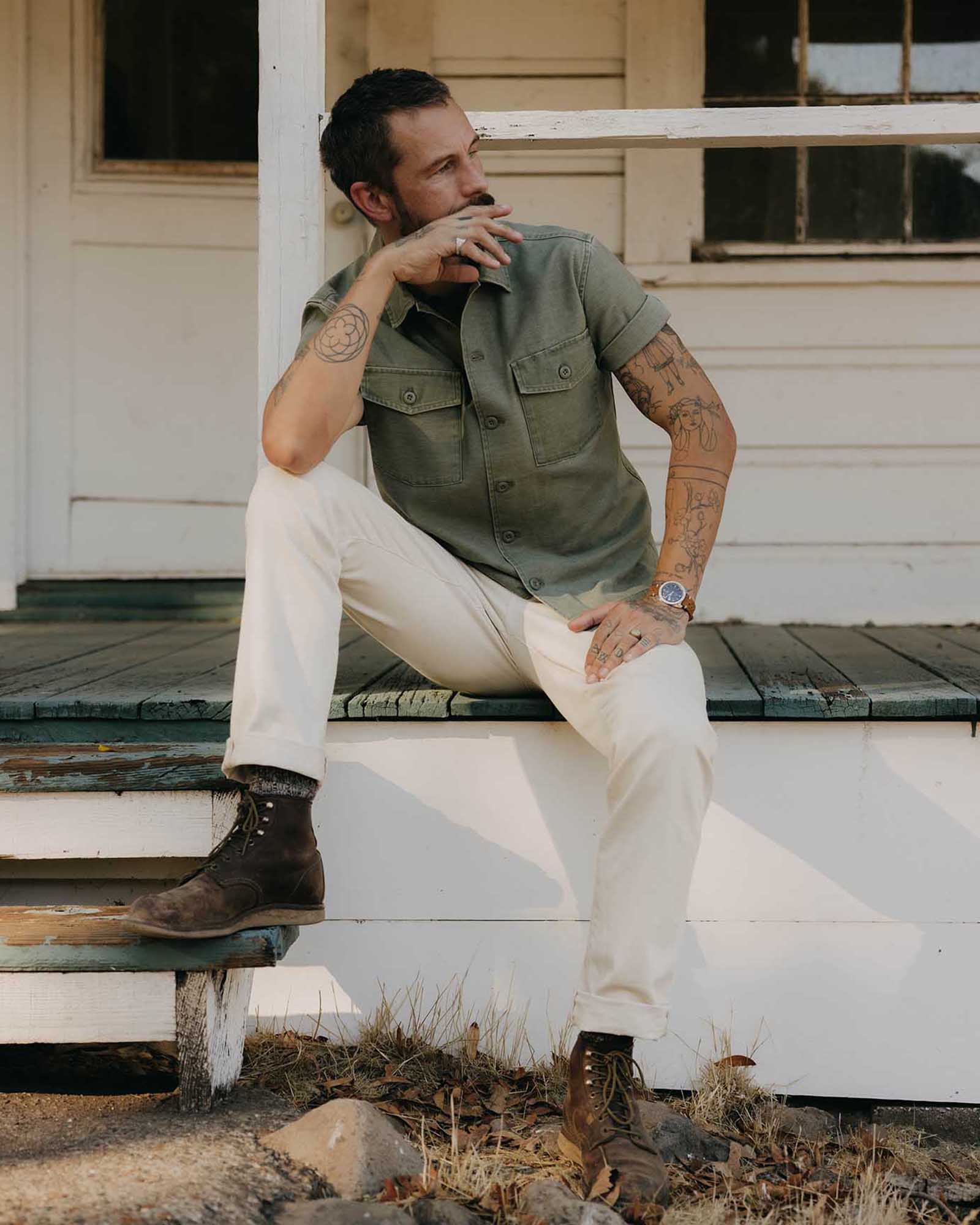 fit model sitting wearing The Short Sleeve Surplus Shirt in Field Olive Reverse Sateen, Wovens by Taylor Stitch