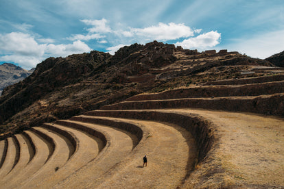 A man standing on one of several large terraces cut into a rocky mountainside.