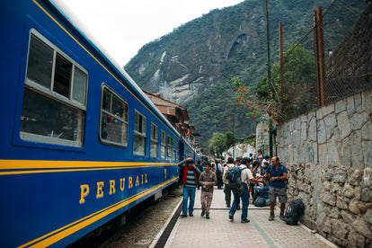 Travellers milling around on a platform next to a parked blue Perurail-liveried train.