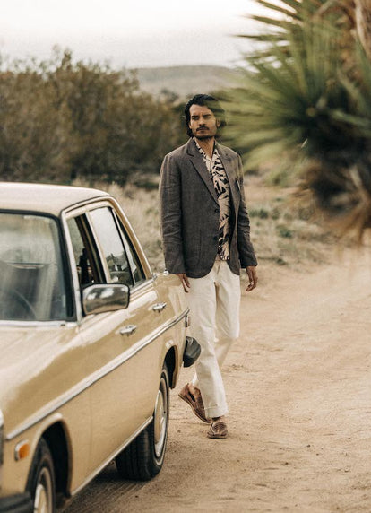 Model walking by a vintage Mercedes in The Sheffield Sport Coat in Cocoa Linen, The Short Sleeve Hawthorne in Dried Palm and The Democratic Jean in Natural Selvage