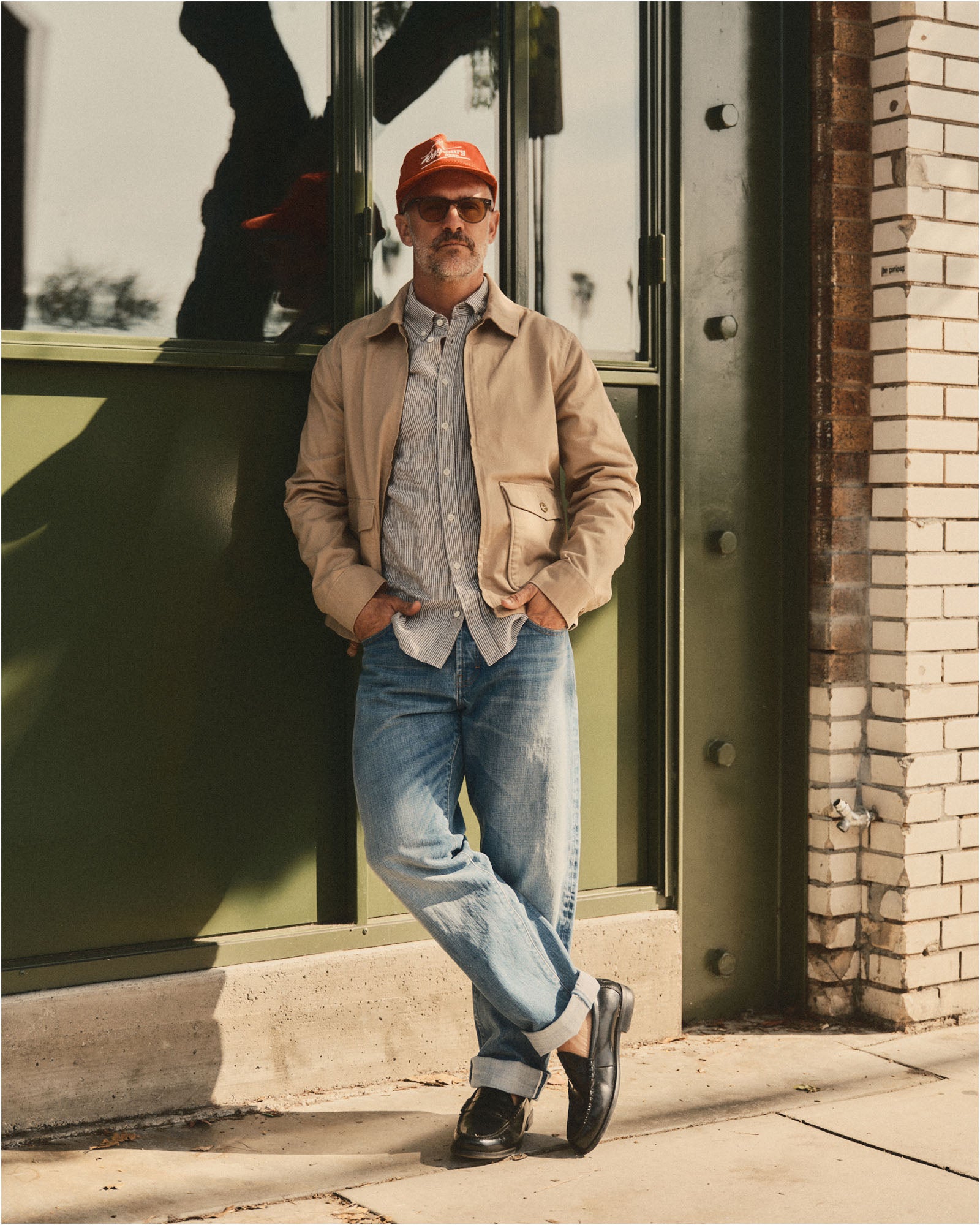 fit model leaning against the wall wearing The Airman Jacket in Organic Khaki Foundation Twill, Outerwear by Taylor Stitch