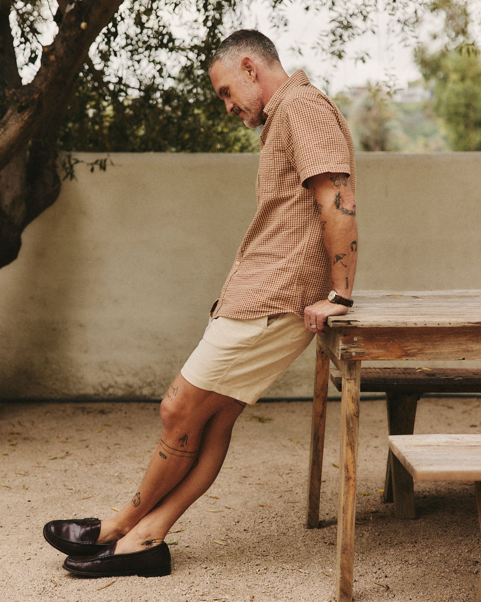 fit model leaning against a table wearing The Short Sleeve Jack in Brick Check Seersucker, Wovens by Taylor Stitch
