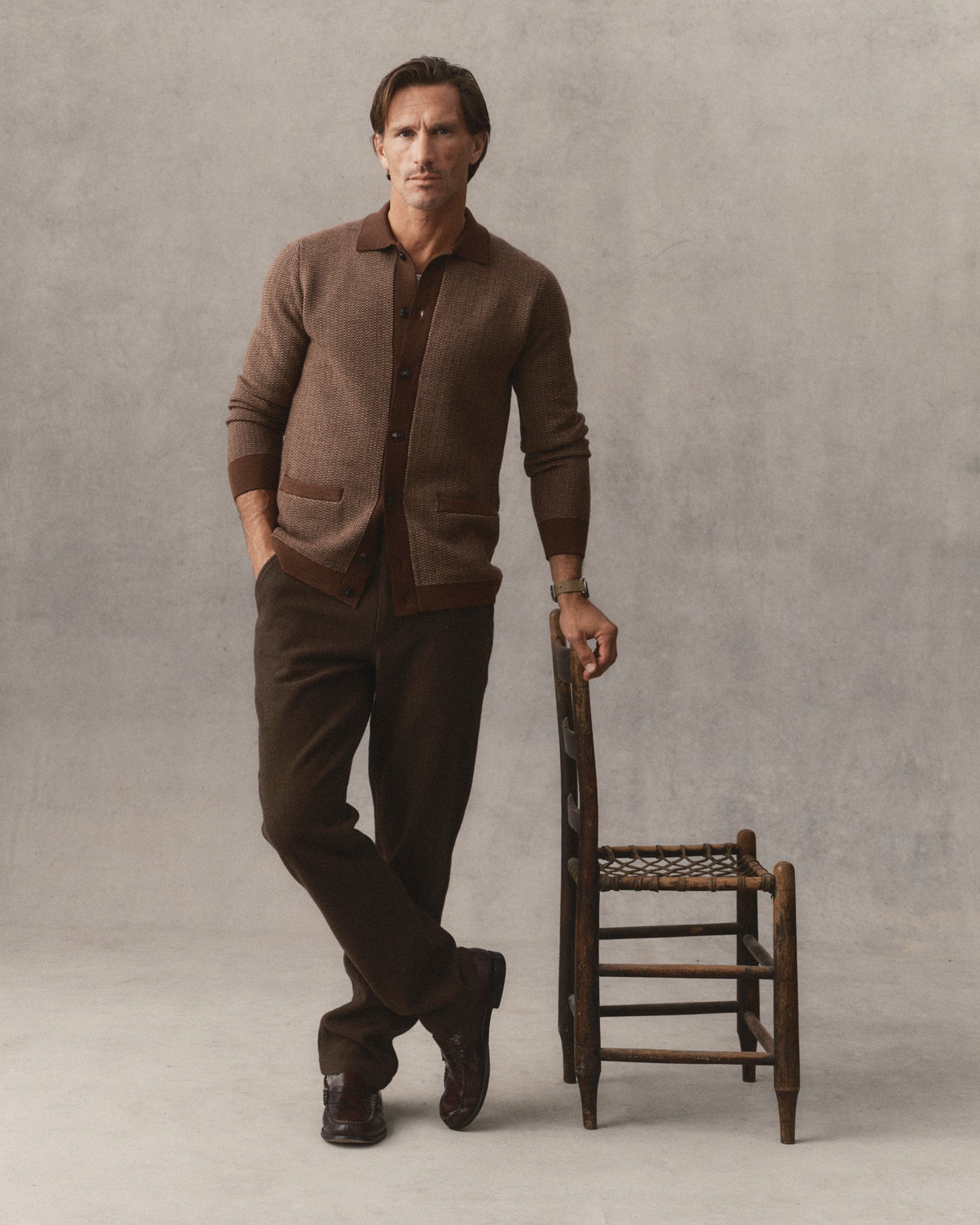 fit model leaning against a chari wearing The Miles Sweater Polo in Espresso Merino, Sweaters by Taylor Stitch
