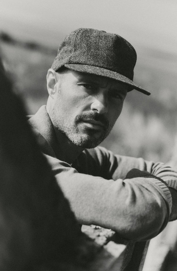 fit model leaning against a fence wearing The Mercer Cap in Walnut Herringbone Wool