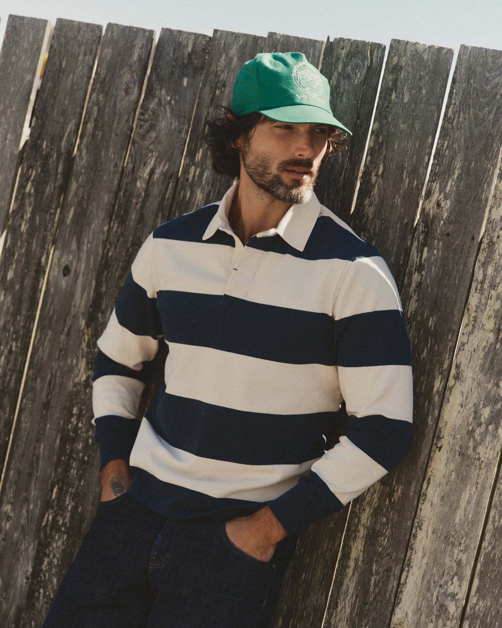 fit model leaning against the wall wearing The Rugby Shirt in Navy Stripe, Knits by Taylor Stitch