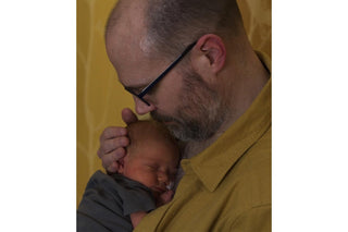 A close-up of a man holding a baby against his chest.