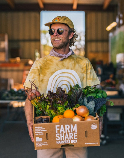 Volunteer wearing The Organic Cotton Tee in Ecology Center while holding a crate of produce