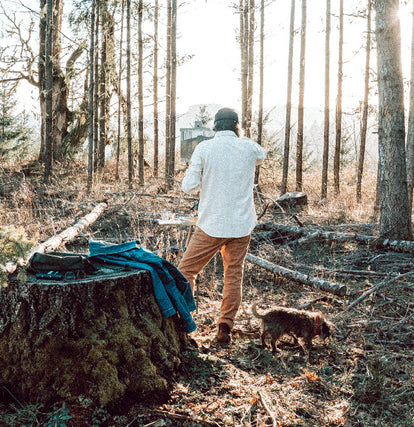Zach wearing The Chore Shirt in Natural Herringbone and The Chore Pant in Tobacco Boss Duck with his dog in the woods.