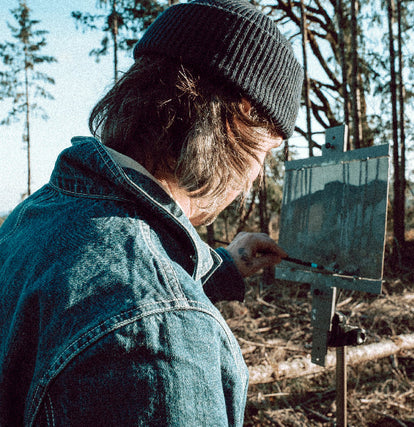 Zach painting a landscape in the woods of the Oregon Coast while wearing The Ojai Jacket in Sawyer Wash. 