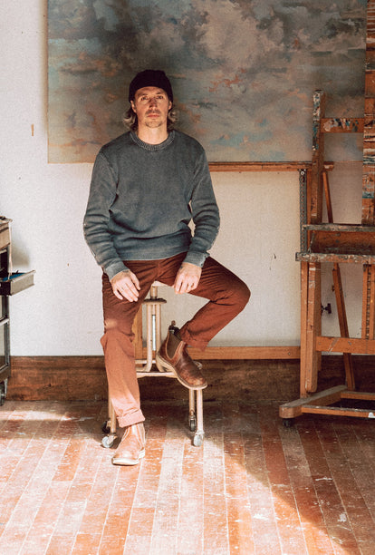 Zach wearing The Moor Sweater in Washed Indigo while sitting in his studio.