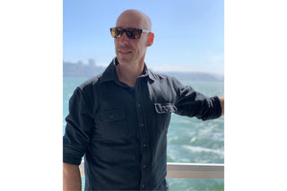 A man in a blue shirt and sunglasses with San Francisco and the bay blurred in the background.