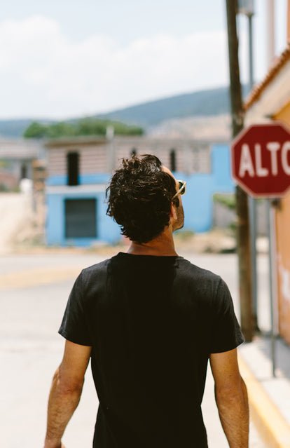 A guy in a black tee, walking towards a sign that reads 'ALTO'.