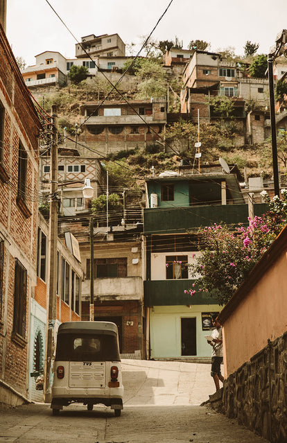 Looking up a steeply sloping street towards a rickshaw and small brick dwellings tightly packed on a hillside.