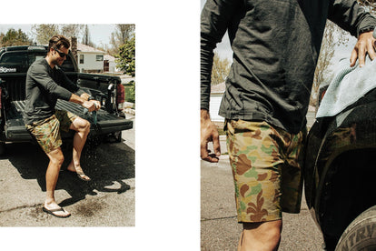 Alex wearing camo-pattern shorts, sitting on the back of a black truck bed in a driveway, wringing out a wet rag.