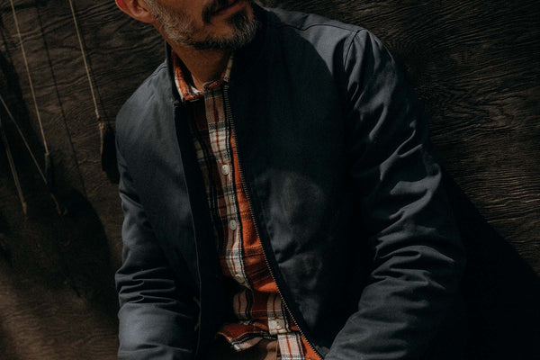 fit model leaning agains the wall wearing The Insulated Bomber Jacket in Dark Navy Dry Wax