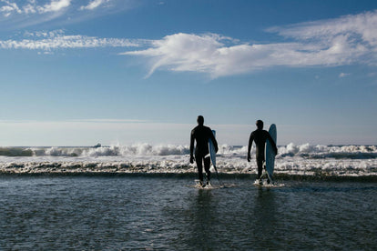 Two surfers walking out into the surf, boards under arms