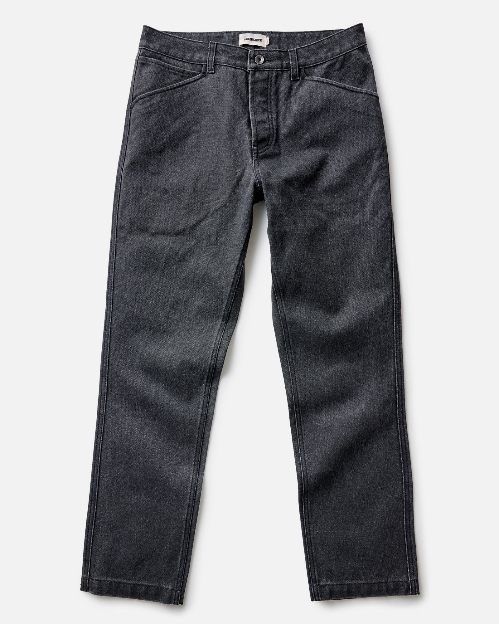 fit model leaning against a wood pile wearing The Camp Pant in Coal Chipped Canvas, Bottoms by Taylor Stitch