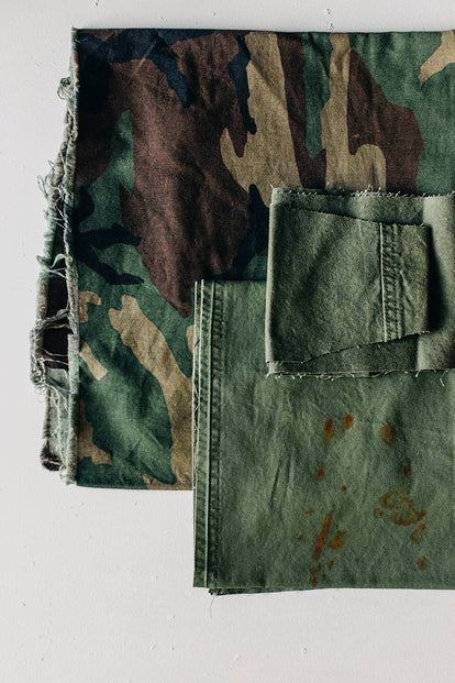 Frayed swatches of olive and camouflage fabrics are stacked together against a white backdrop.