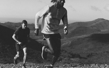 Black and white photo of two guys running, with mountain scenery in the background.