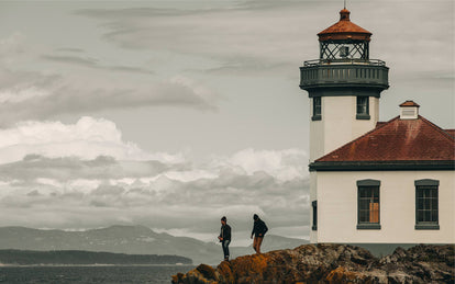 Two men looking over the water at a lighthouse.