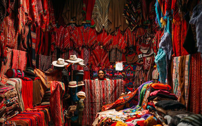 A stall ownder holding up red patterned fabric, surrounded by much similar fabric, festooning the walls.
