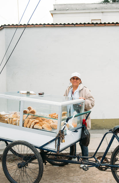 A woman standing behind a rickshaw with a perspex case mounted on it, containing baked goods.