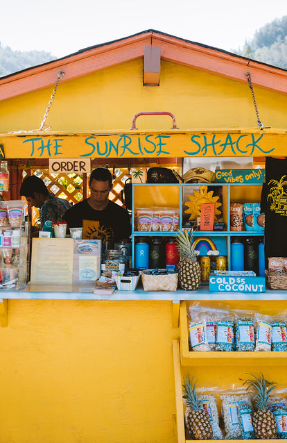 Staff at yellow-painted wooden counter, topped with pineapples; The Sunrise Shack.