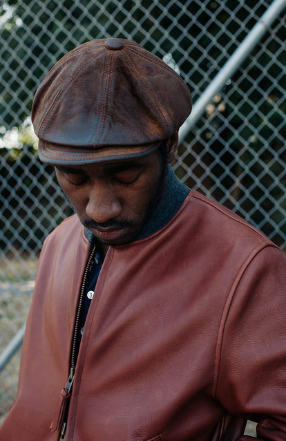 Head and shoulders of man wearing cap, looking down at the jacket he is wearing.