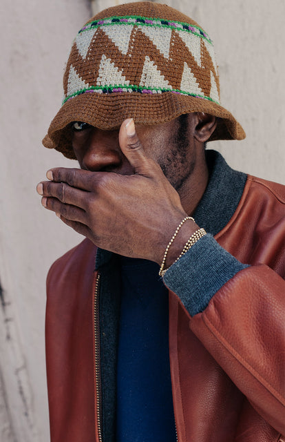 Our guy covering his mouth, looking out from under the brim of his hand-made hat.
