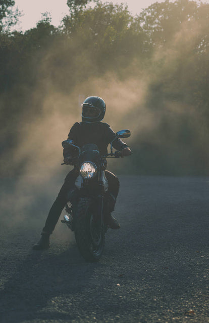 A faded front-on shot of a man on a motorcycle, stopped with one leg on the ground, out to the side.