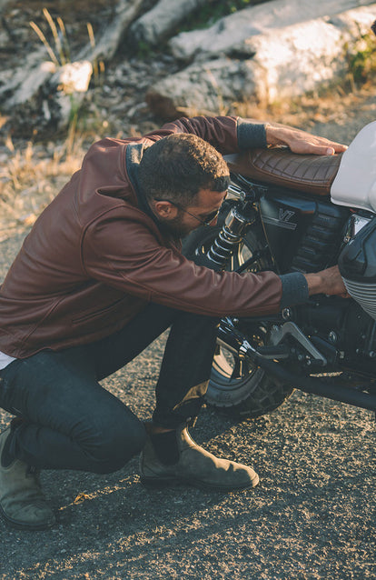 Making some adjustments to the engine on a motorcycle, wearing a brown leather jacket.