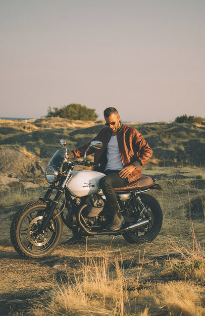 A man on a motorbike, stopped, checking his pocket, off road.